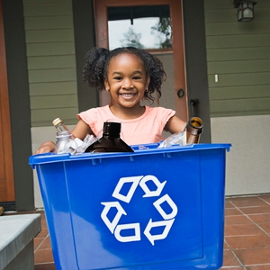 young child smiling holding a bin of recycling